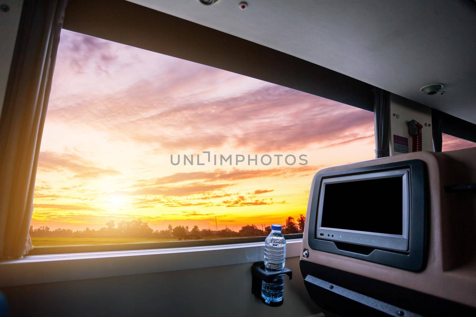 Inside of the bus which has LCD screen blank rear seat for entertainment with a bottle of water and window view of Beautiful landscape nature with sky cloud sunset, Figure tourism road trip concept.