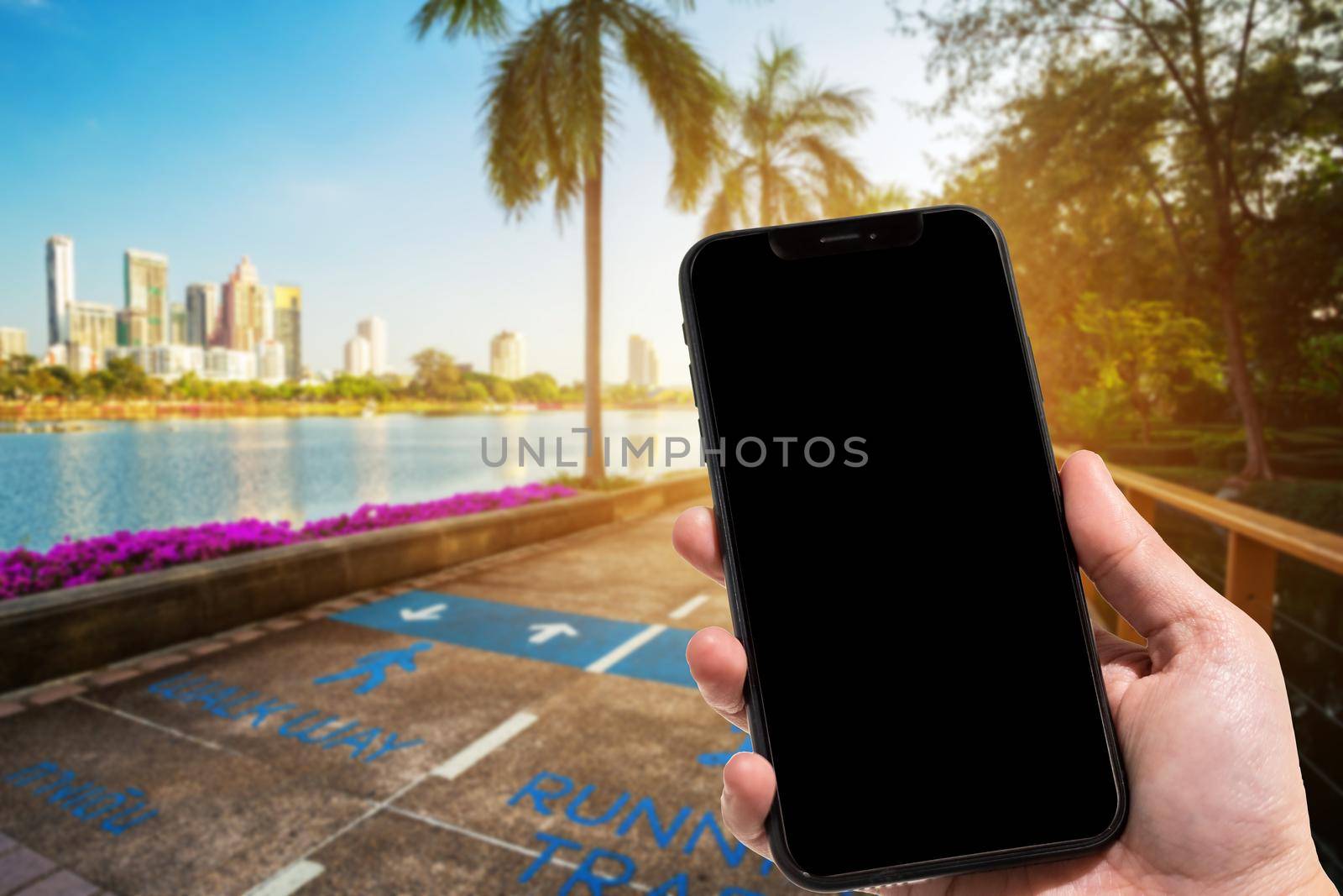 Close-up of female use smartphone blurred images in road pathway in the park for relaxing walking jogging or ride bicycle and exercise at Cityscape blur of the background.