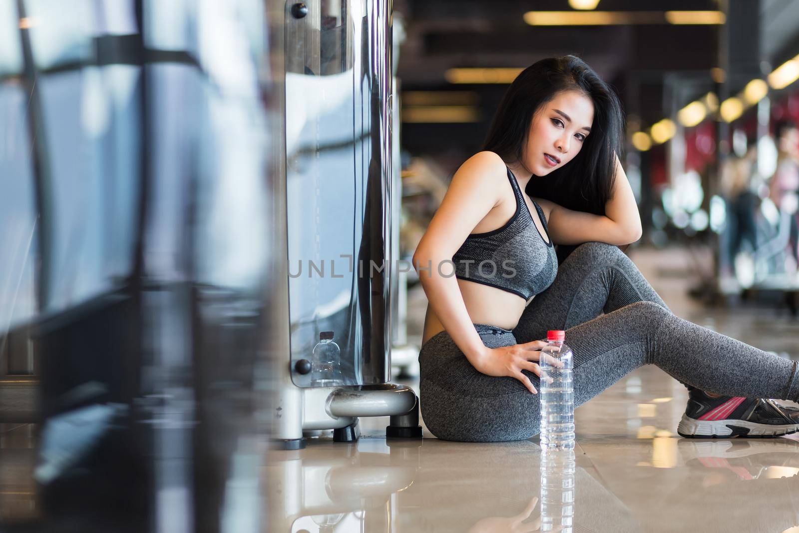 Fitness Asian women sitting in sport gym interior and fitness health club with a bottle of water.