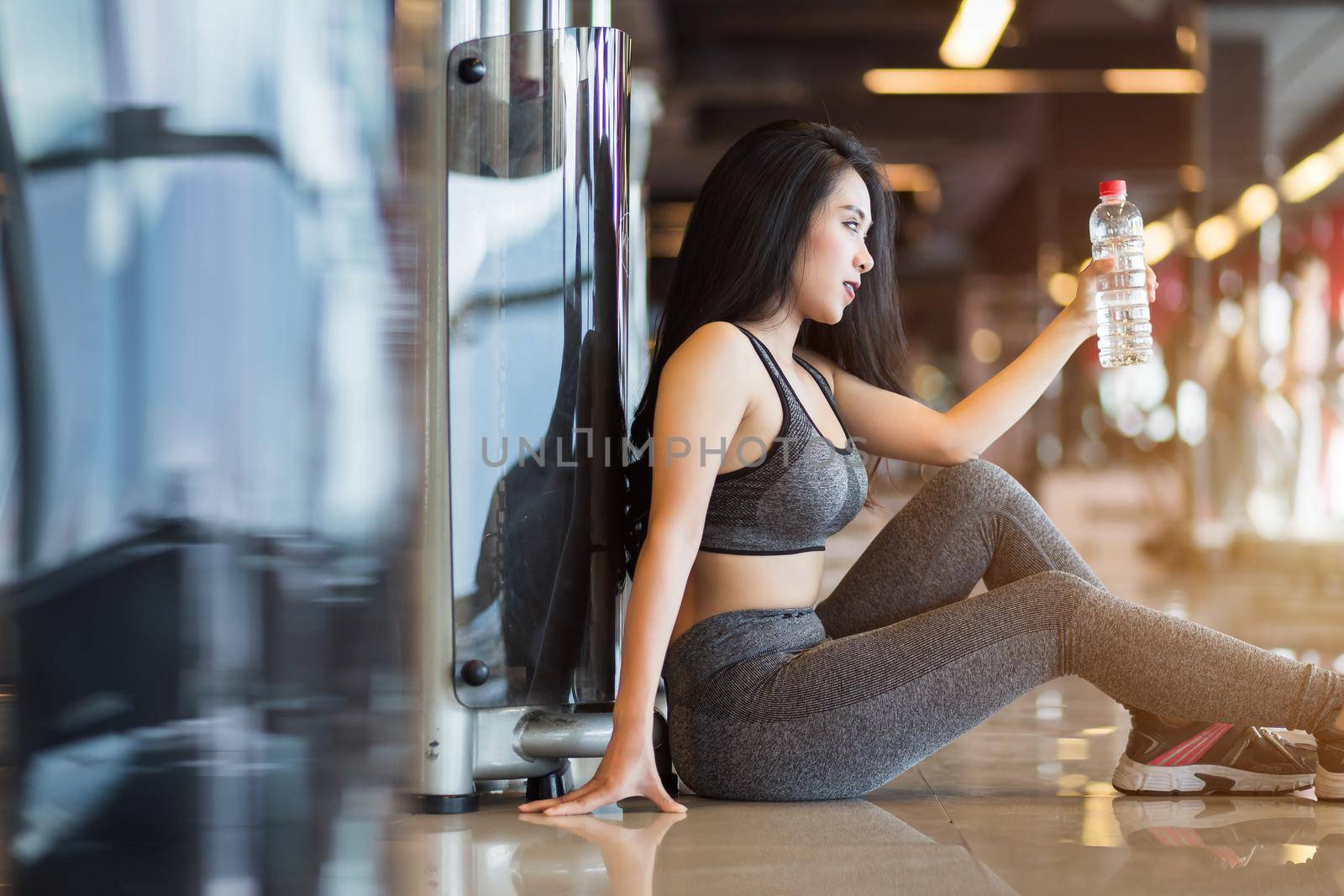 Fitness Asian women sitting in sport gym interior and fitness health club with a bottle of water. by tinapob2534