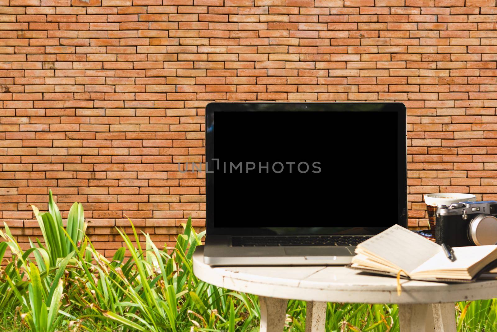 Mockup image of laptop with blank black screen with camera,notebook,coffee cup on wooden table with wall large texture background.