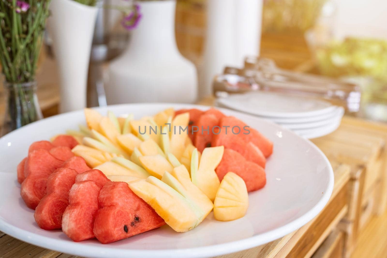 Chop the pieces of watermelon and pineapple in white dish the dining and flower vase on table decorationat buffet self service at hotel.