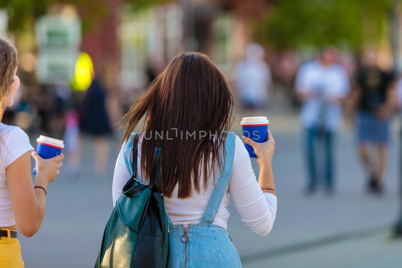 Two girlfriends of the girl are walking down the street and drinking from a glass of coffee.