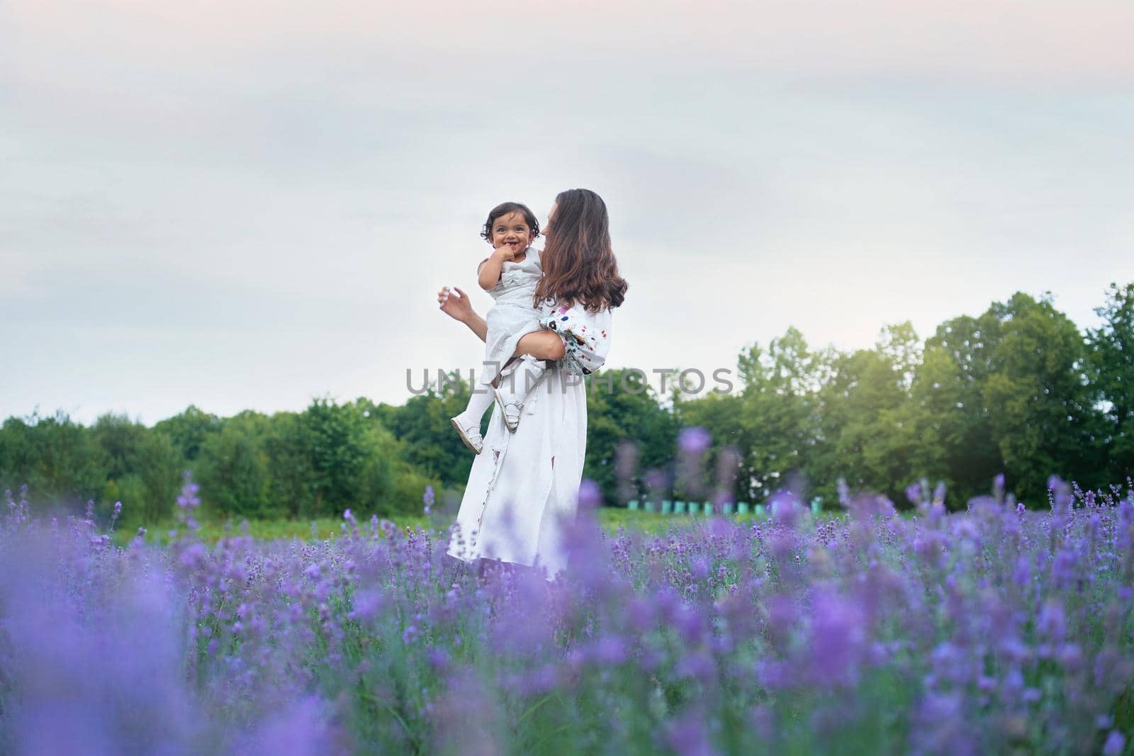 Mother carrying laughing baby and lavender bouquet. by SerhiiBobyk