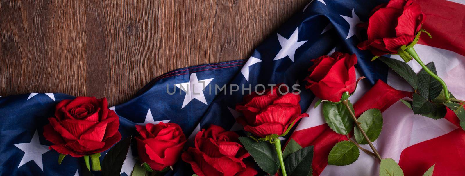 Concept of U.S. Independence day or Memorial day. National flag and red rose over dark wooden table background.