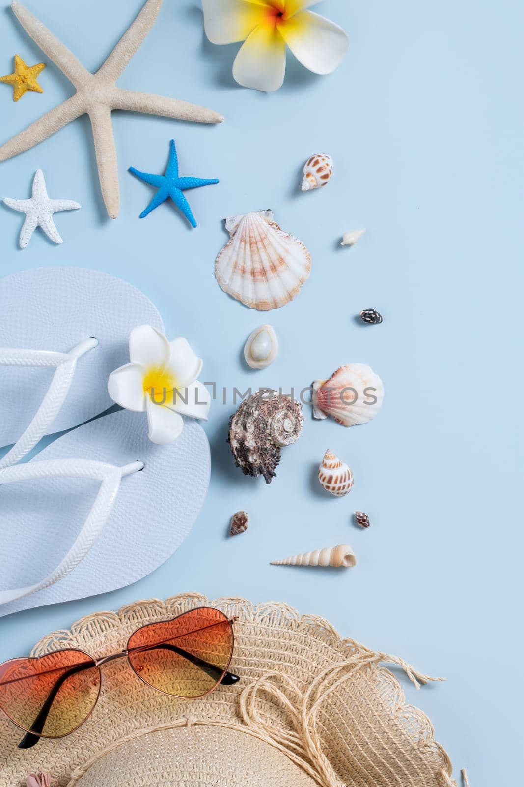 Summer beach background design concept. Top view of holiday travel with shells, hat, slipper on blue background.