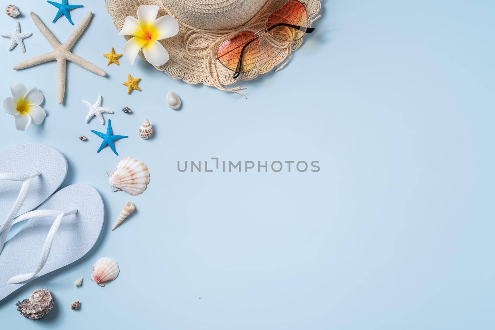Summer beach background design concept. Top view of holiday travel with shells, hat, slipper on blue background.