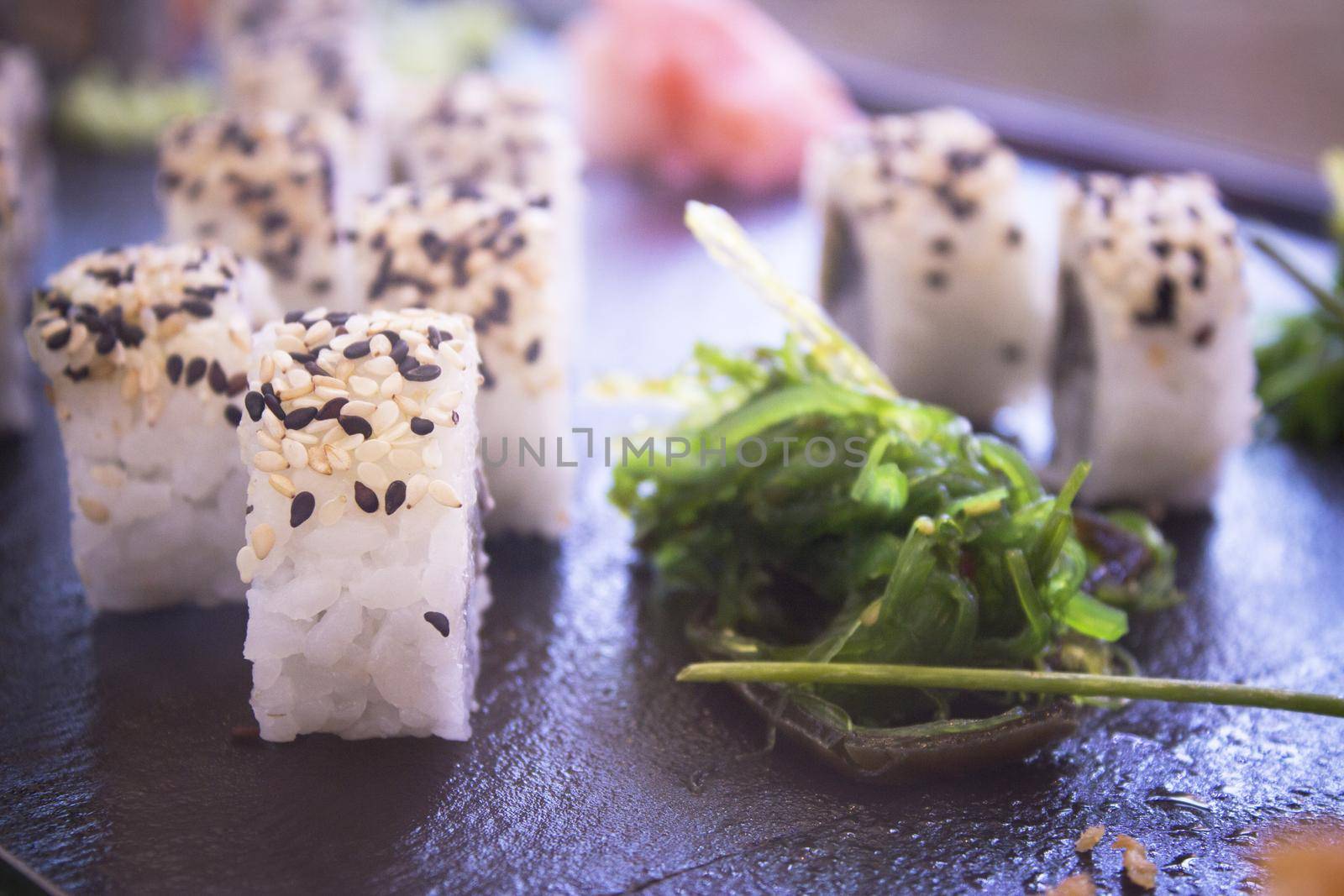 Assorted sushi food on a black slate plate. No people