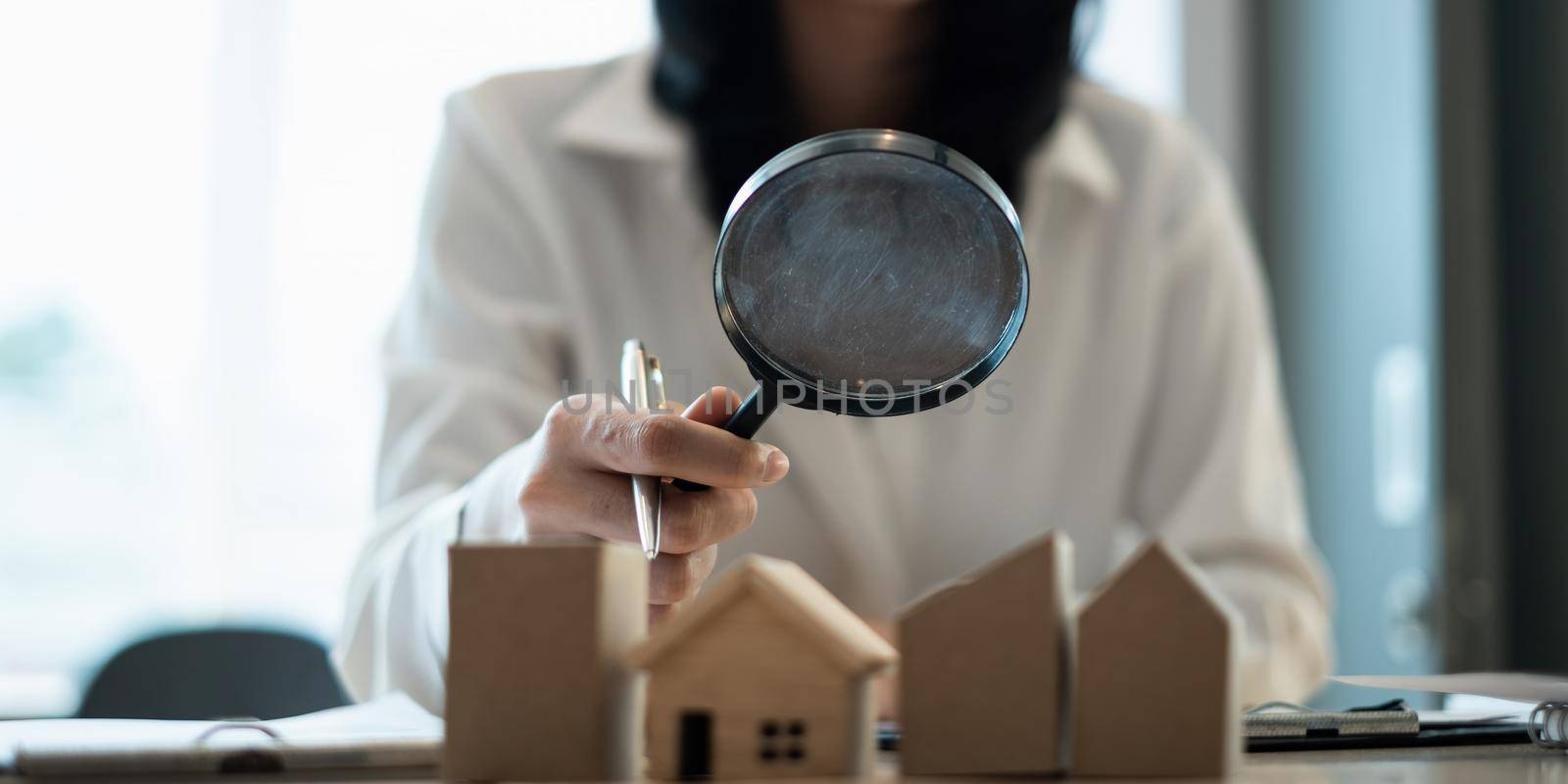 A woman holding magnifying glass and checking house model .Real Estate House Appraisal And Inspection concept. by itchaznong