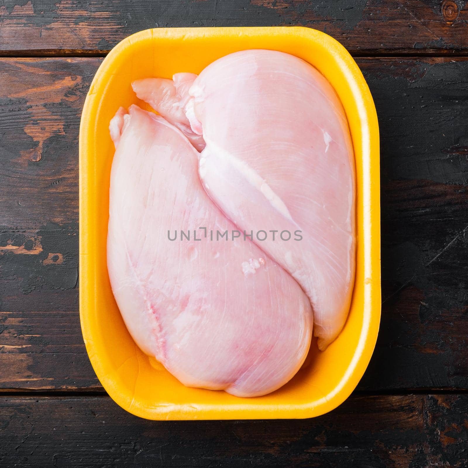 Fresh chicken breast meat in open tray, on dark wooden background