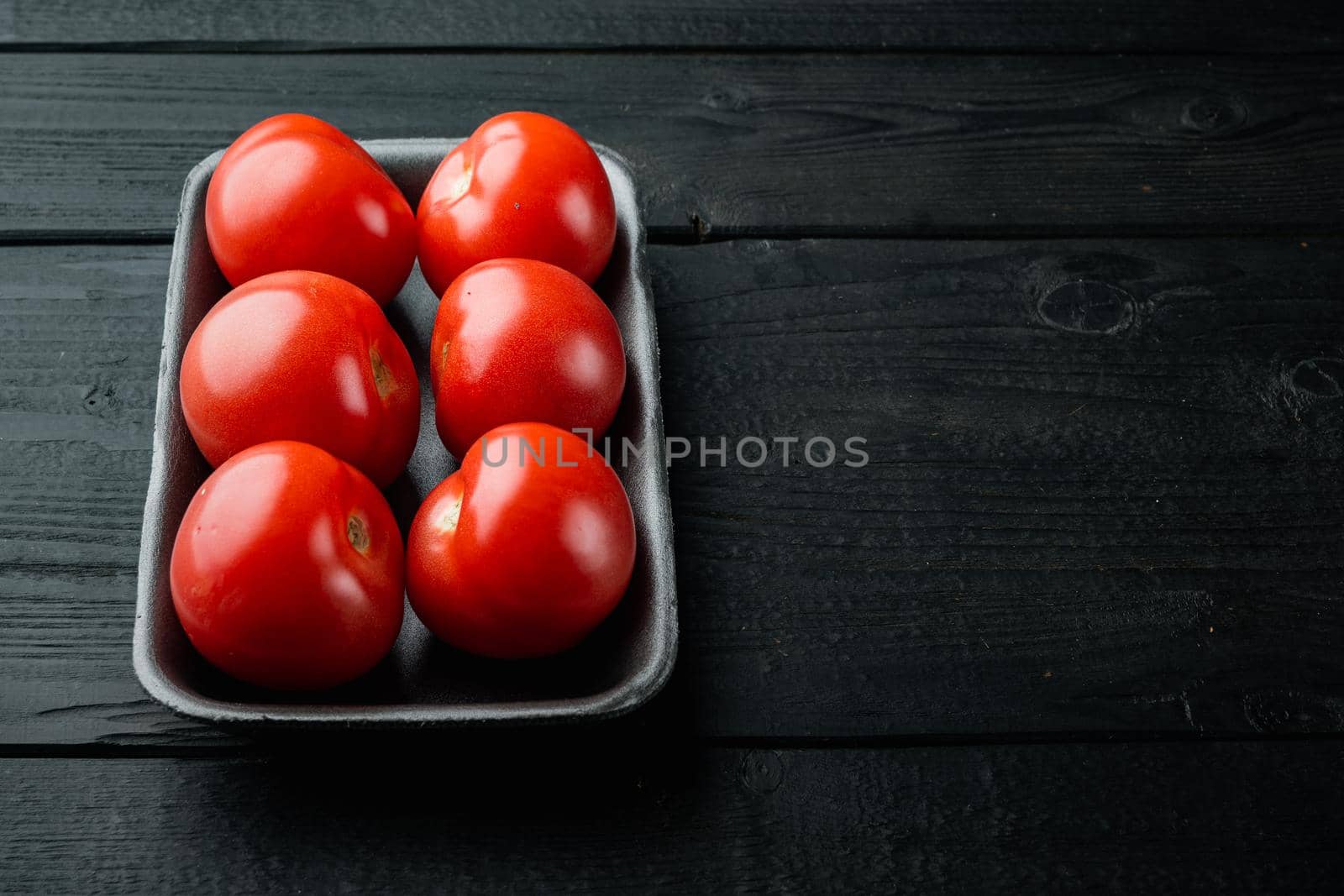 Red tomatoes, on black wooden table with copy space for text