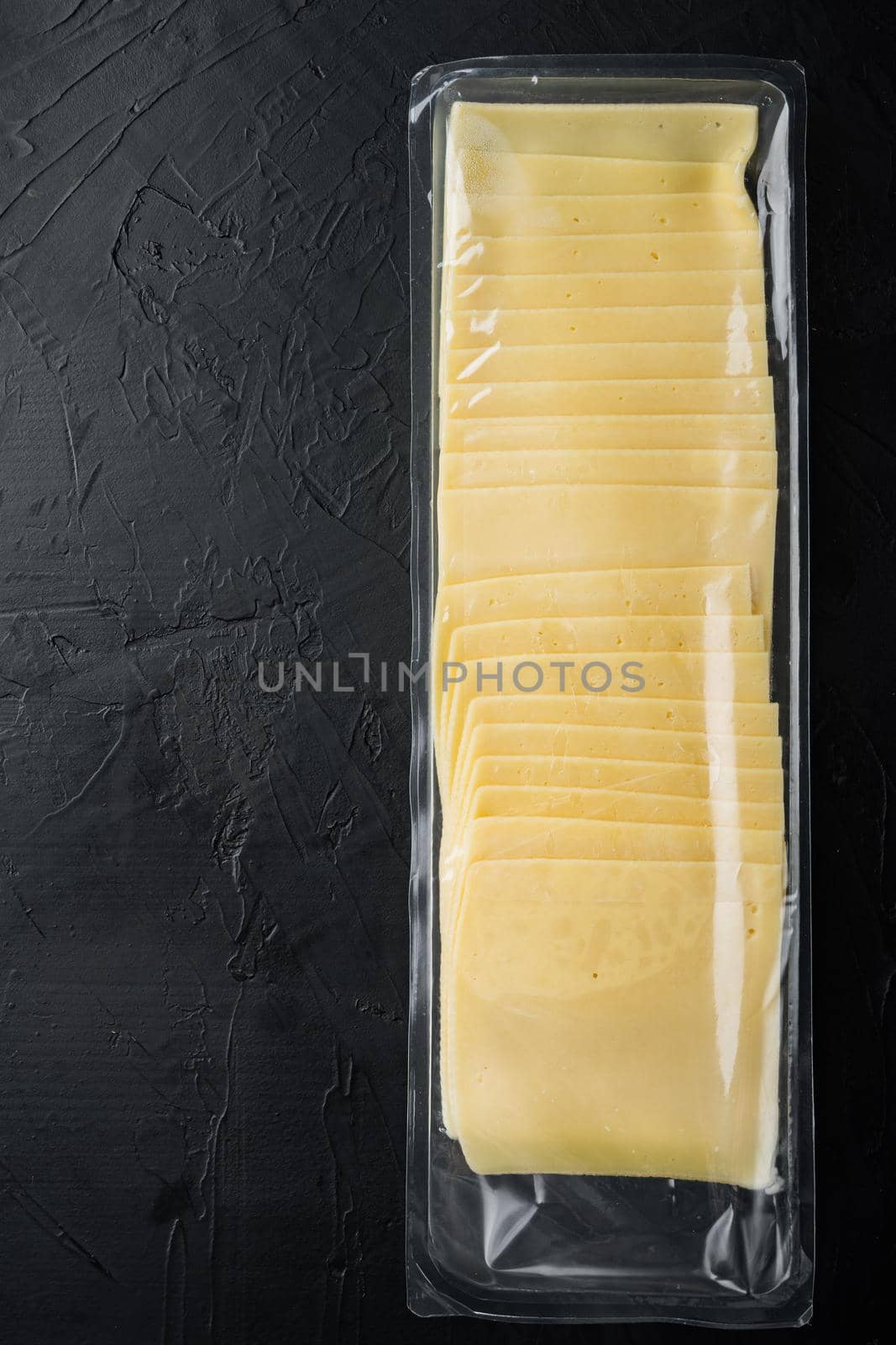 Slices of yellow cheese, sealed pack, on black background with copy space for text