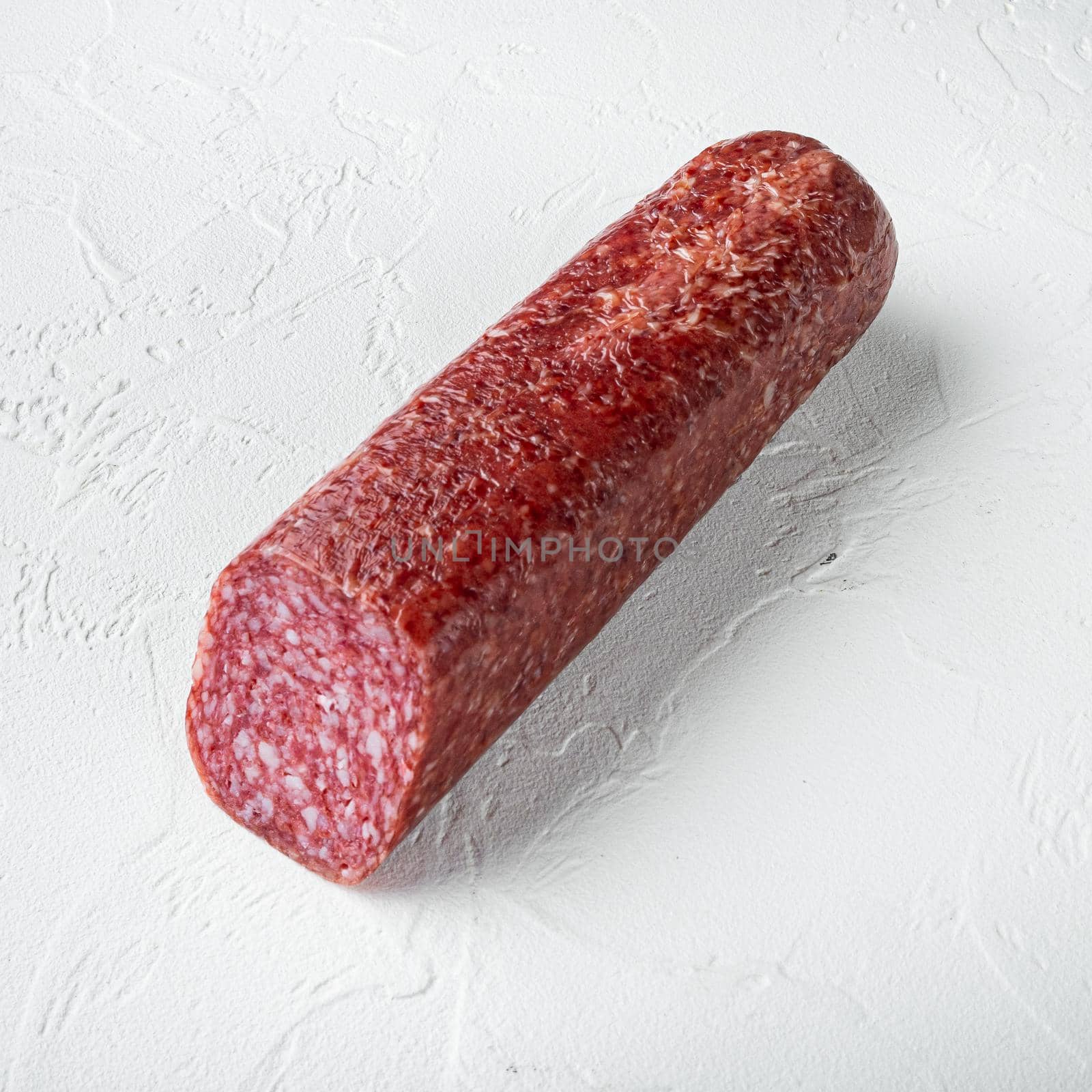 Traditional smoked salami sausage with spices, square format, on white stone table background by Ilianesolenyi