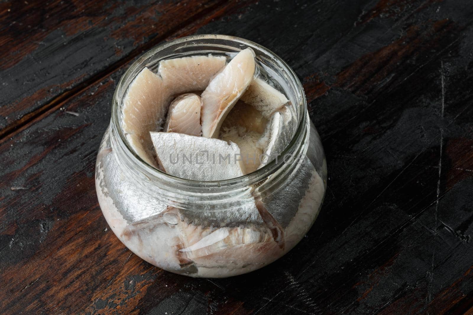 Canned Wild Herring Fillets set, in glass jar, on old dark wooden table background, with copyspace and space for text