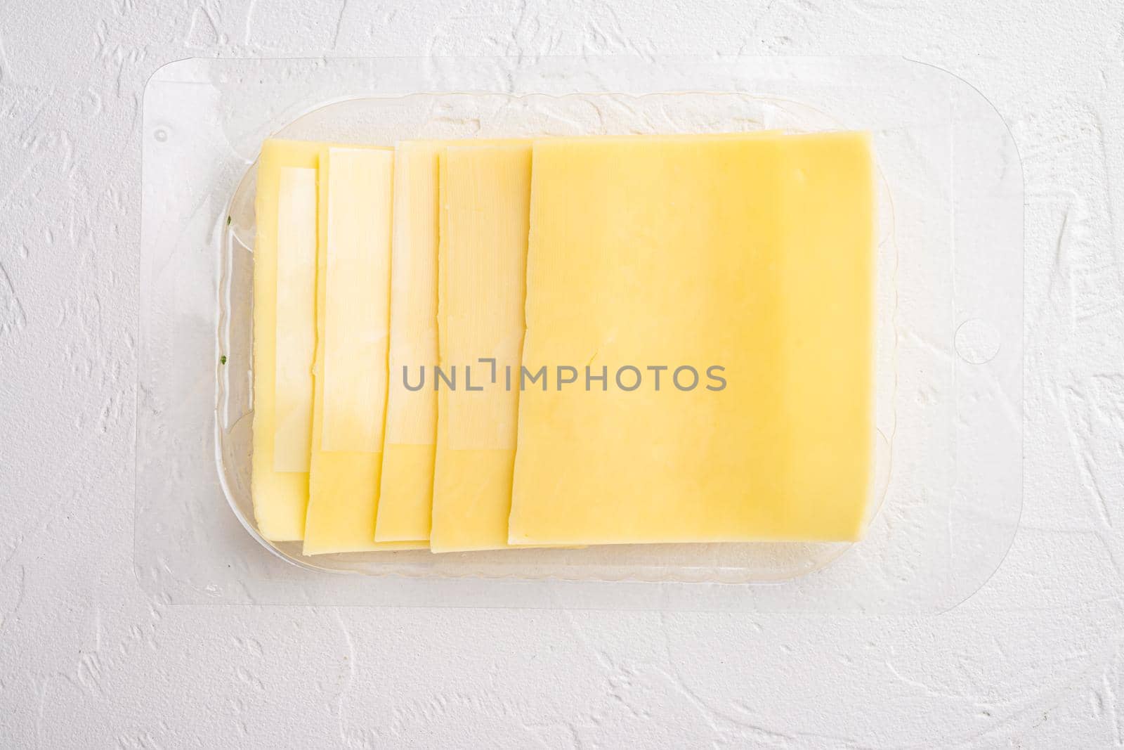 Pieces of Cheddar cheese set, in plastic pack, on white stone background, top view flat lay