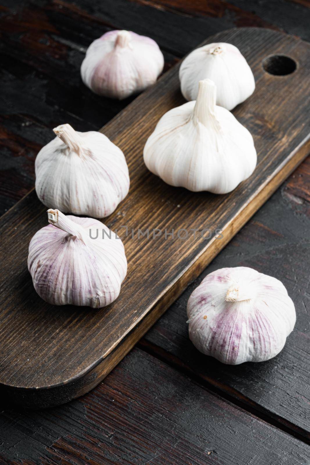 Pile of organic farm garlic set, on wooden cutting board, on old dark wooden table background
