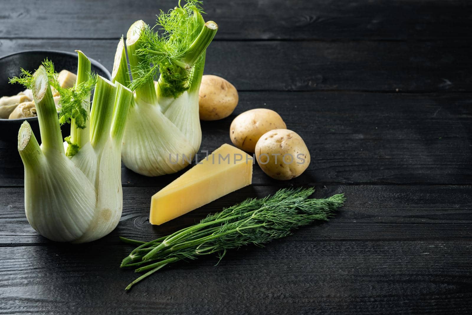 Artichoke with fennel, potato and parmesan ingredient, on black wooden table with space for text
