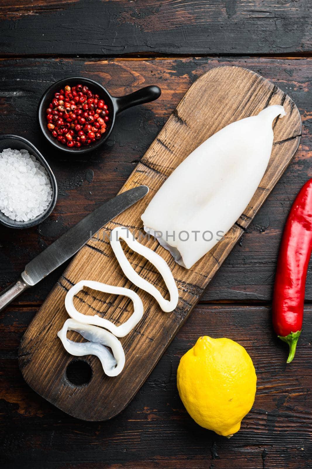 Raw squid, sliced for rings on cutting board with lemon and pepper over dark rustic wooden background, flat lay, food photo.