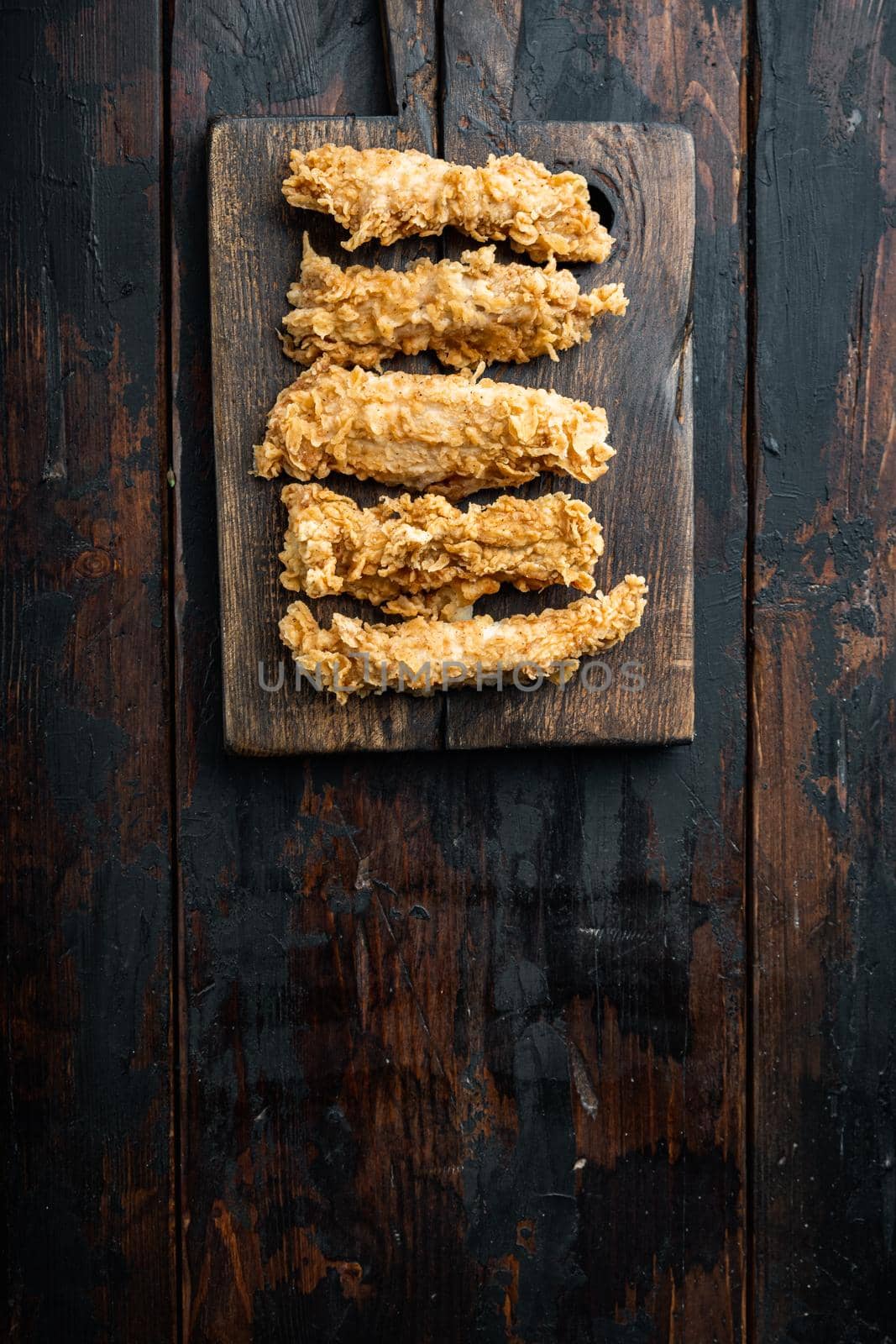 Chicken breaded breast fillet on dark wooden background, flat lay, with space for text.