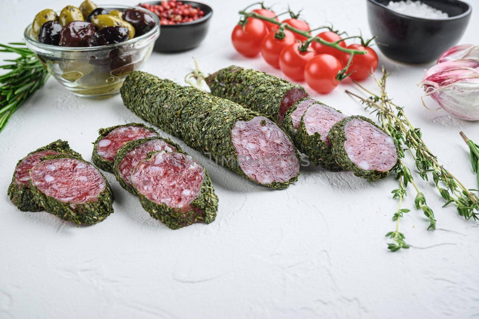 Traditianal fuet sausage in herbs with ingredients on white textured background.