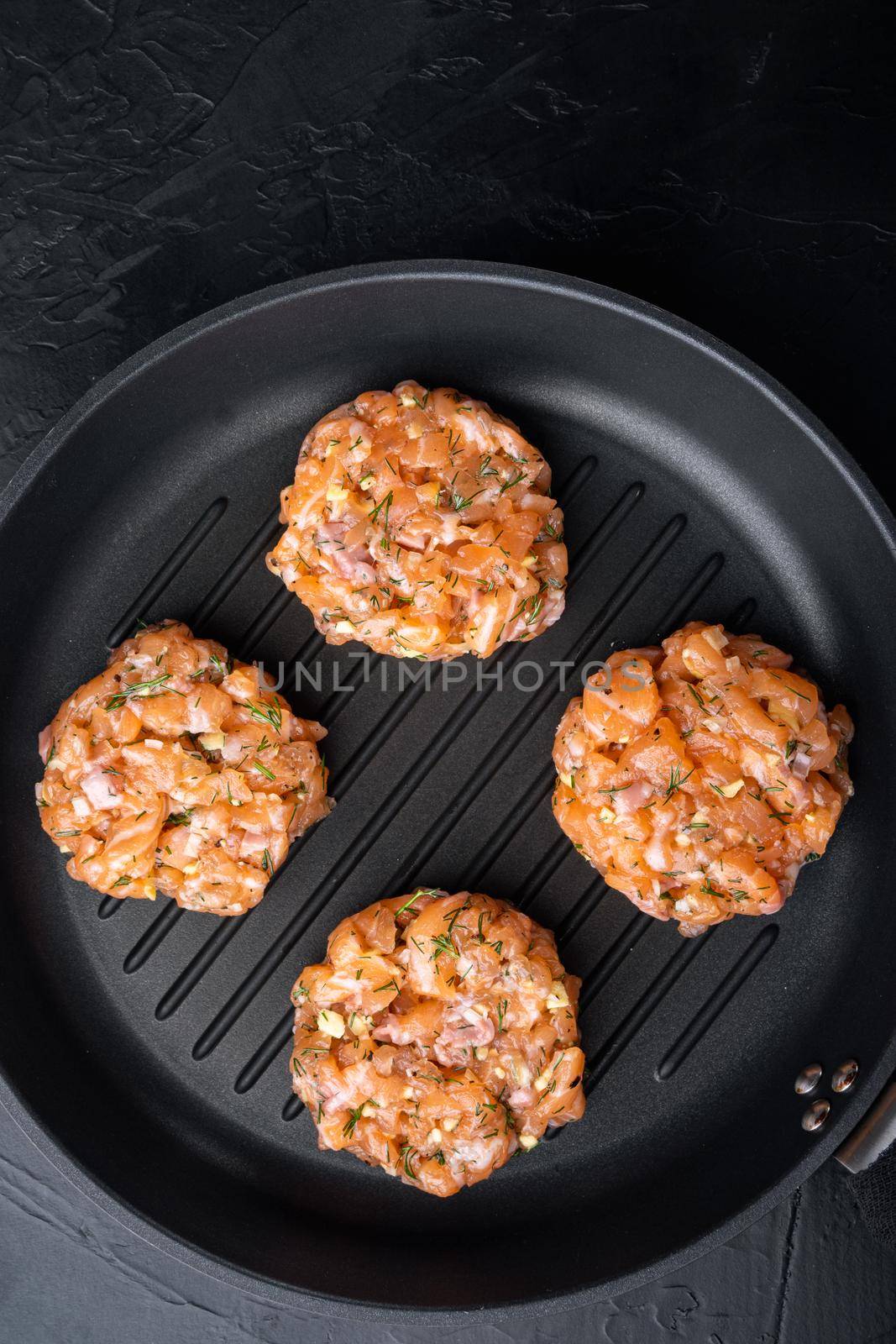 Raw fish patties with salmon fillet and lemongrass, on black textured background, flat lay