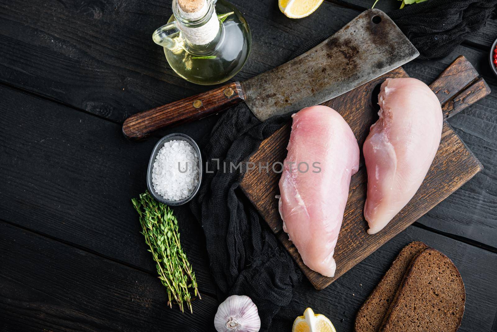 Crumbed uncooked chicken breasts ingredient with butcher knife on black wooden table, flat lay with space for text