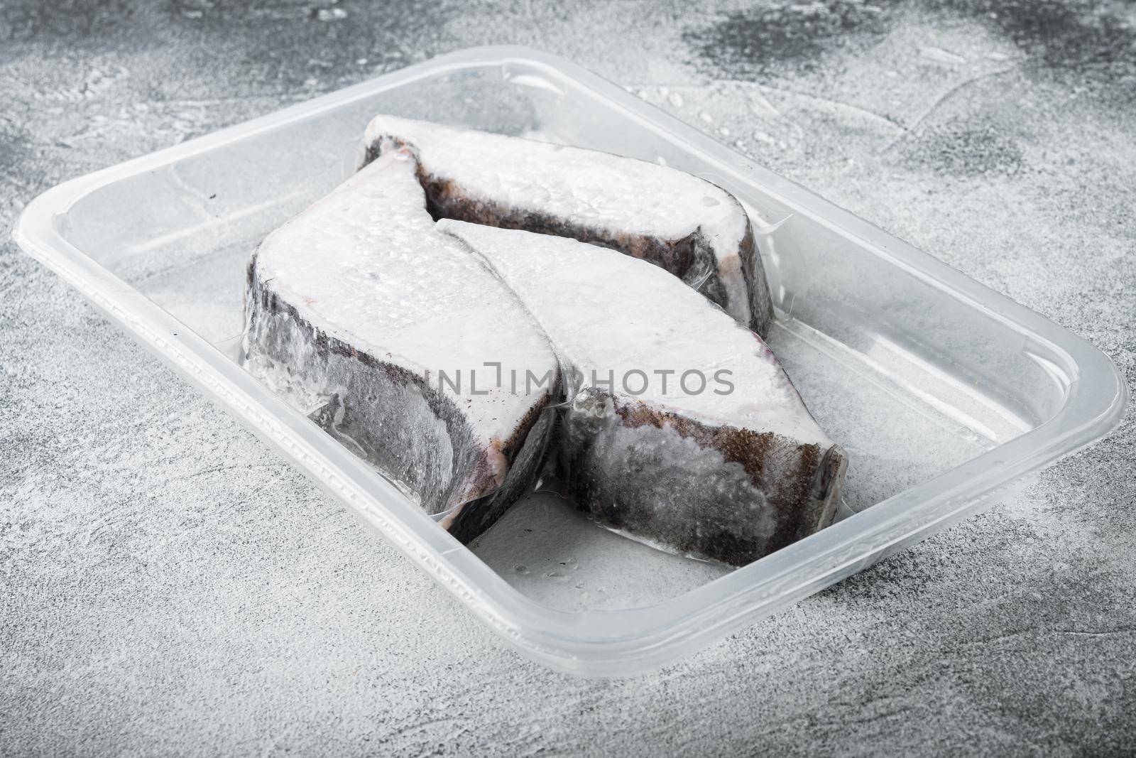 Frozen Greenland halibut steaks vacuum pack set, on gray stone table background, with copy space for text