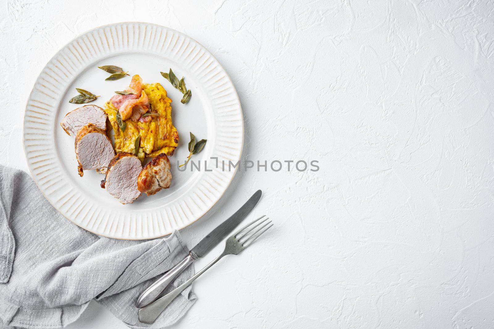 Grilled pork fillet and mash potatoe gratin with sage and prosciutto set, on plate dish, on white stone background, top view flat lay , with copyspace and space for text