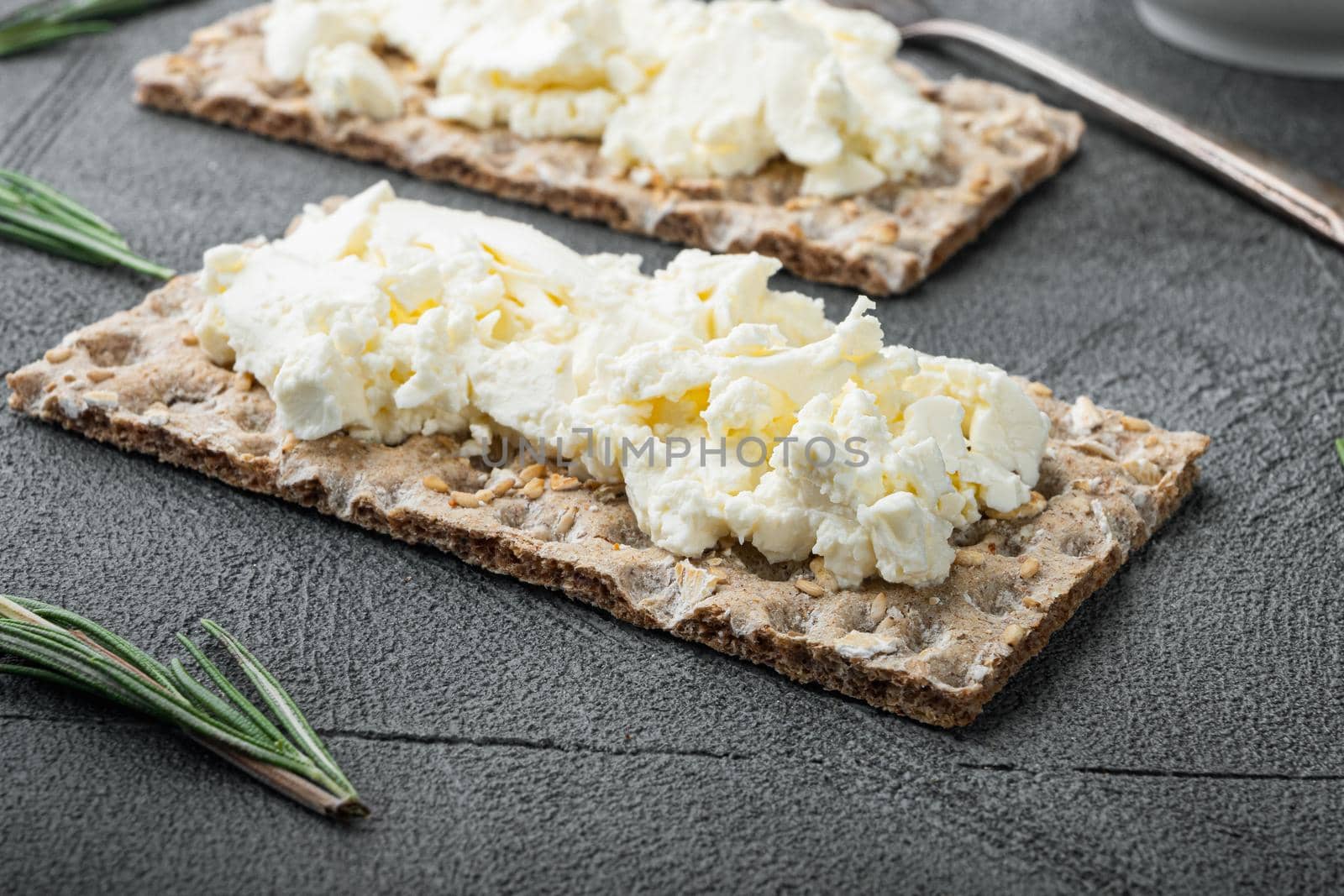 Fresh rye crispbreads with cream cheese set, on gray stone table background