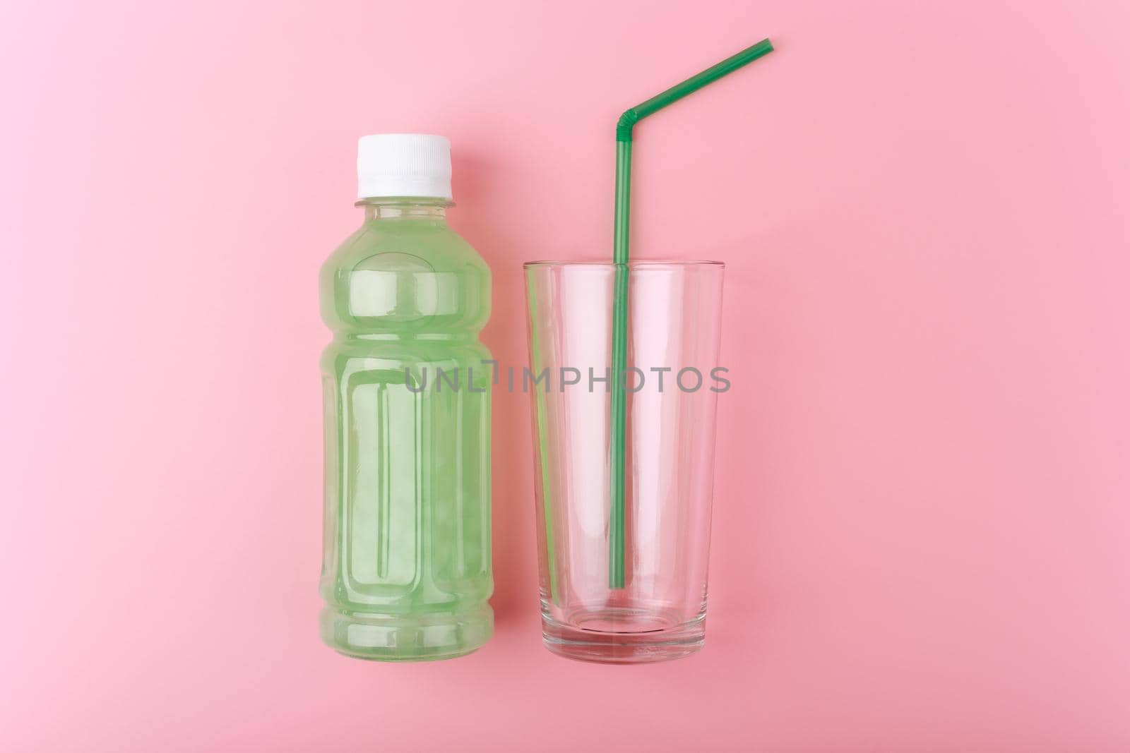 Creative flat lay with transparent plastic bottle with light green detox drink next to empty glass with green straw on bright pink background. Concept of weight loss, dieting and clean eating