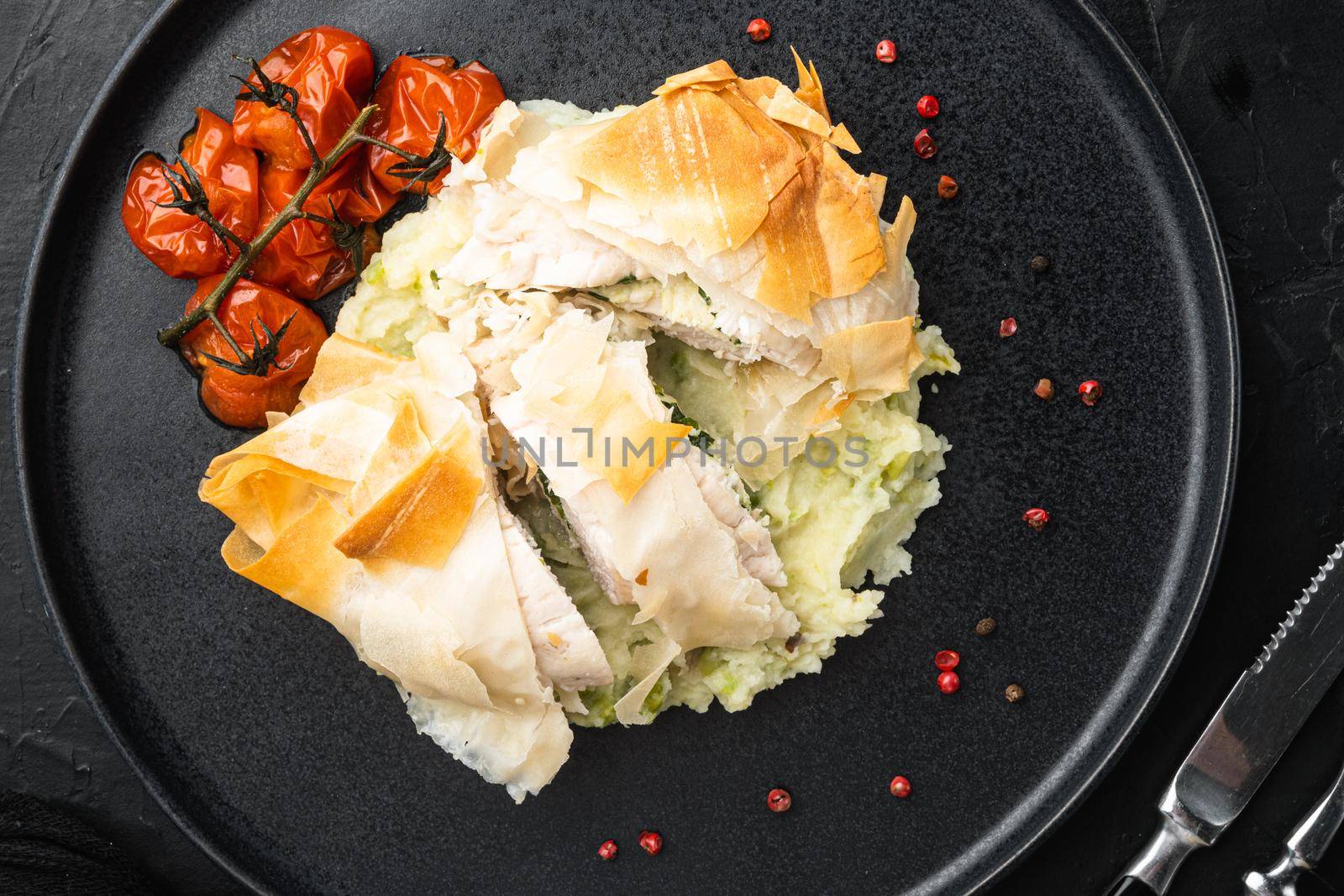 Freshly cooked Chicken Kiev oozing garlic and parsley butter set, with baked cherry tomatoes, mashed potatoes, on black stone background, top view flat lay
