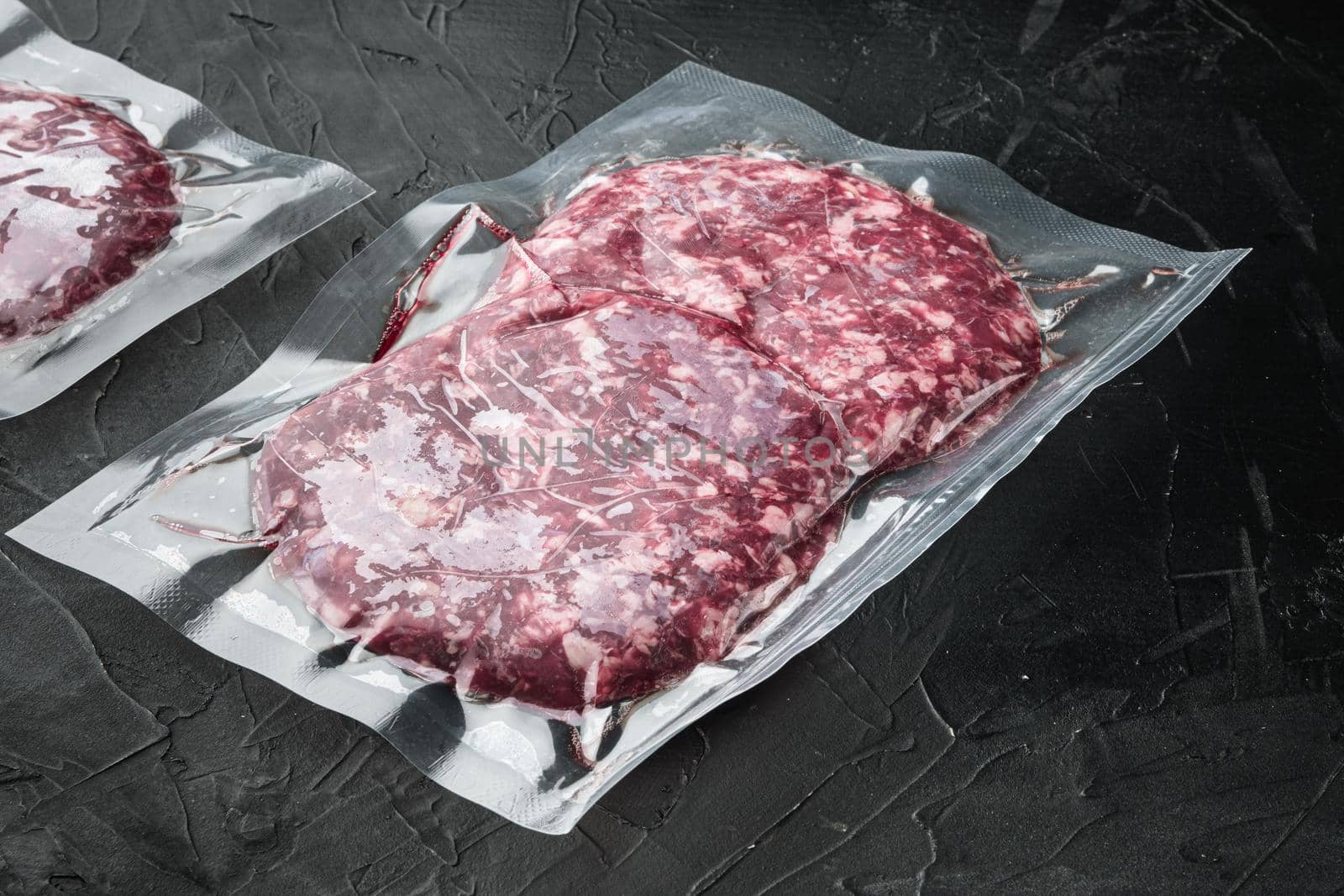 Raw fresh beef burgers minced meat in plastic tray set, on black stone background, with copy space for text