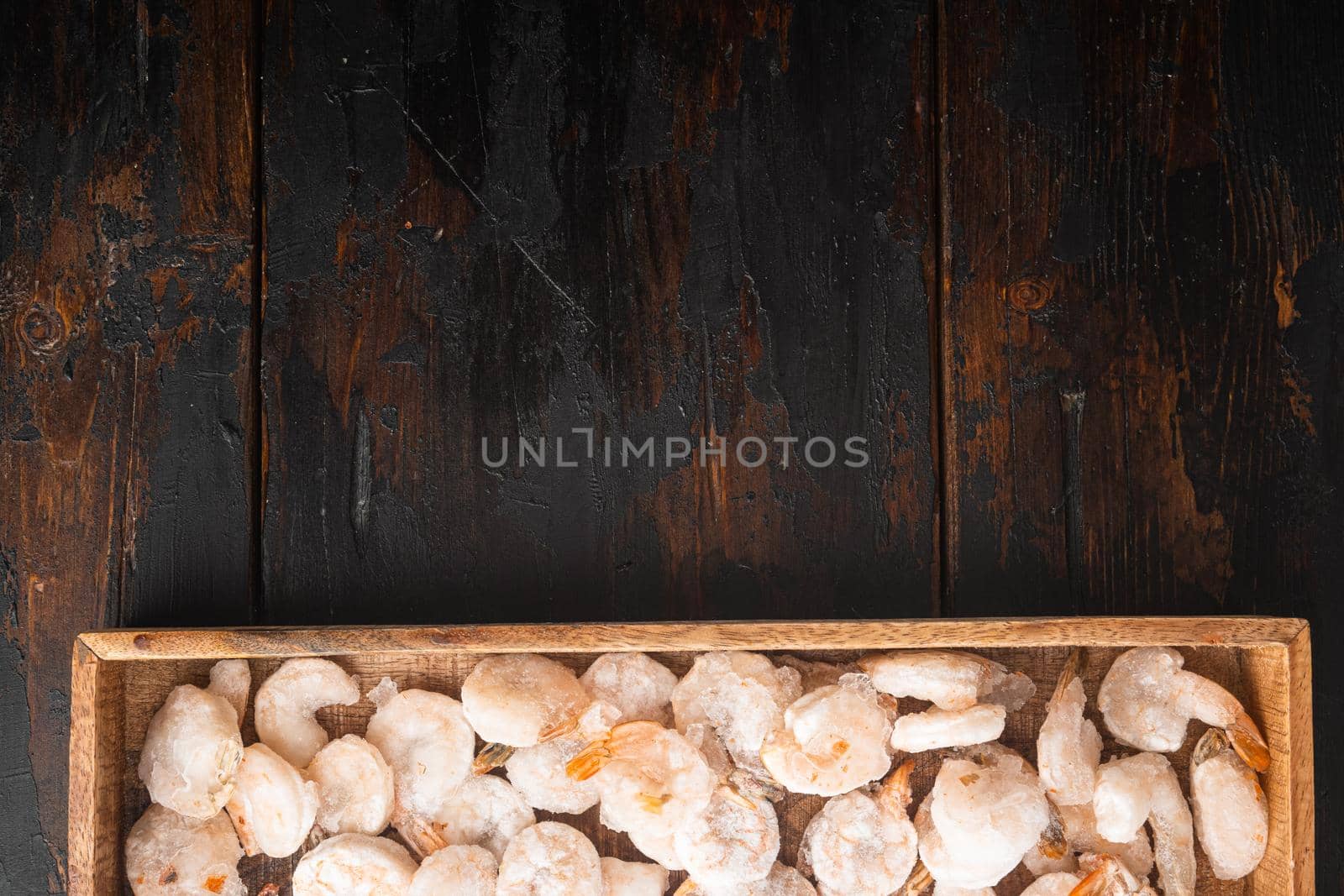 Frozen peeled boiled prawns set, in wooden box, on old dark wooden table, top view flat lay, with copy space for text