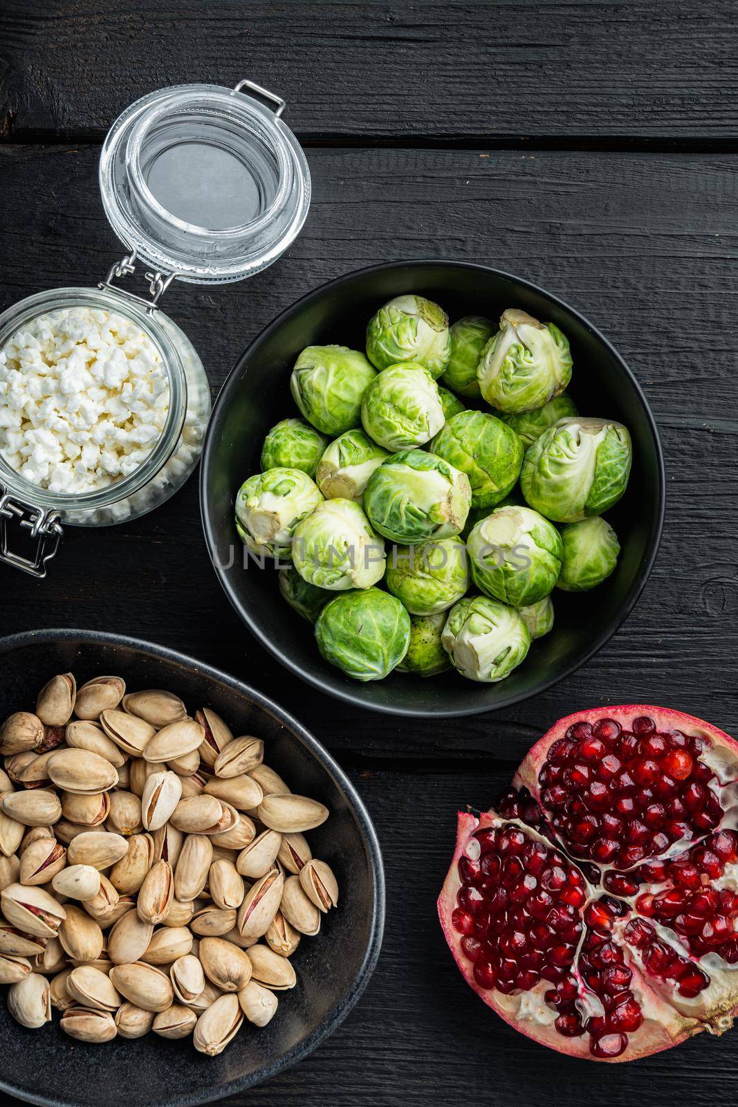 Brussels sprouts with pomegranate, cottage cheese and pistachios, on black wooden table, flat lay
