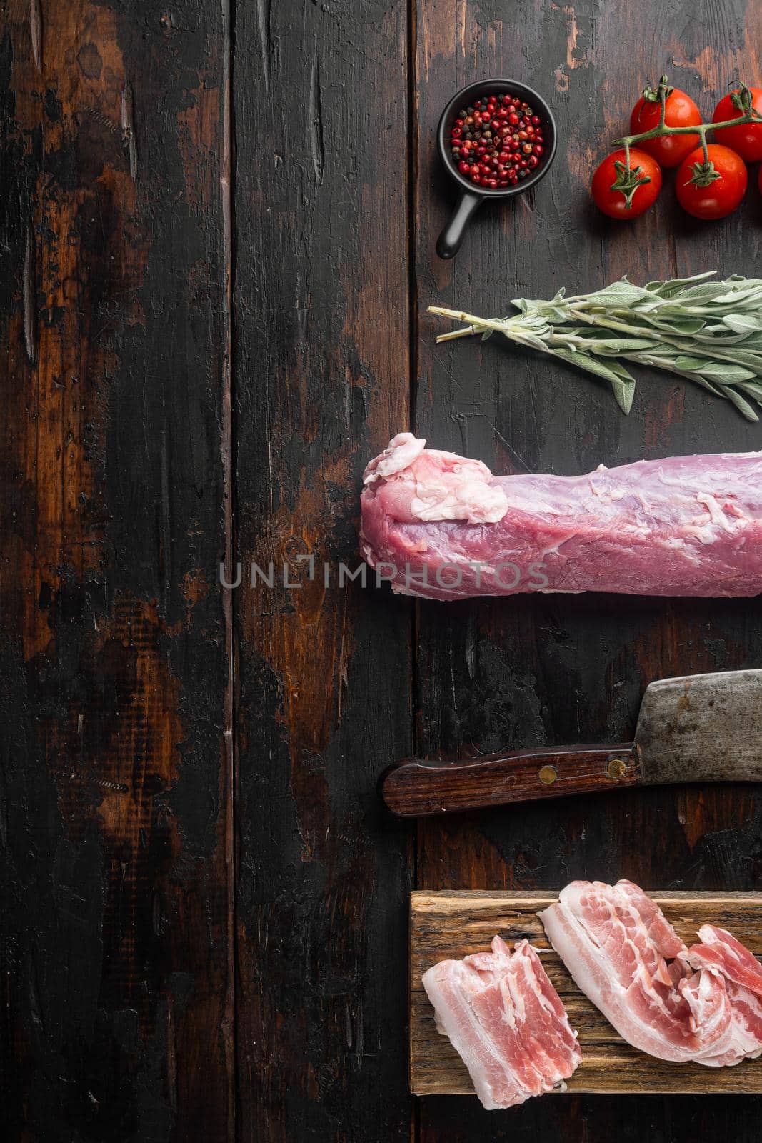Raw pork loin with ingredients and herbs for baking, sage, potatoe set with old butcher cleaver knife, on old dark wooden table background, top view flat lay , with copyspace and space for text