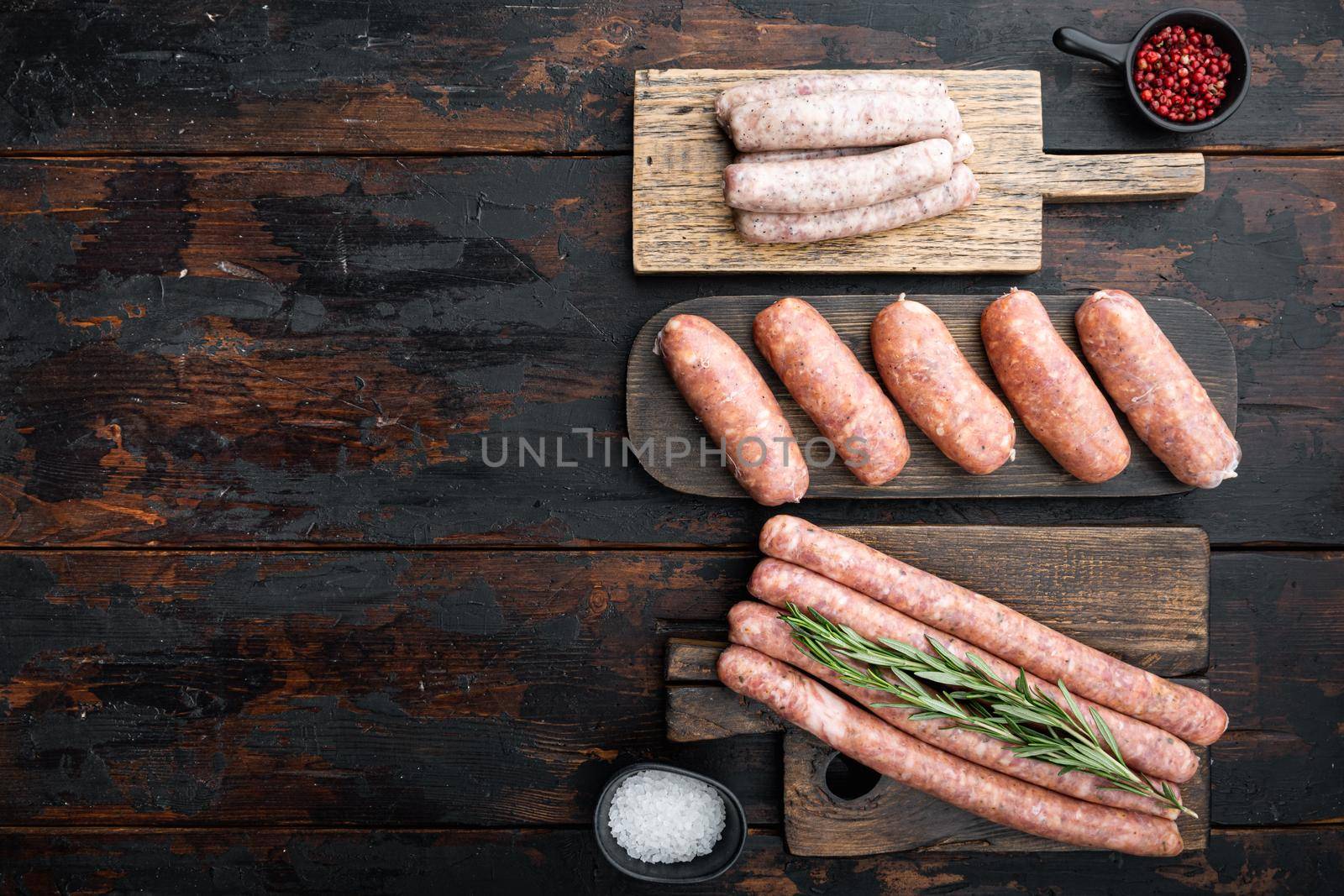 Fresh raw pork, beef and chicken sausages, top view with space for text, on old dark wooden background.