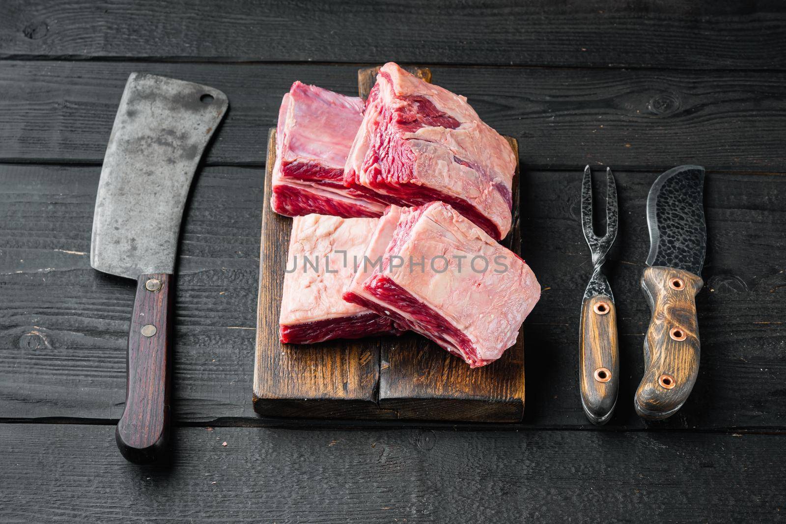 Raw Organic Beef Short Ribs Ready to Cook set, and old butcher cleaver knife, on black wooden table background