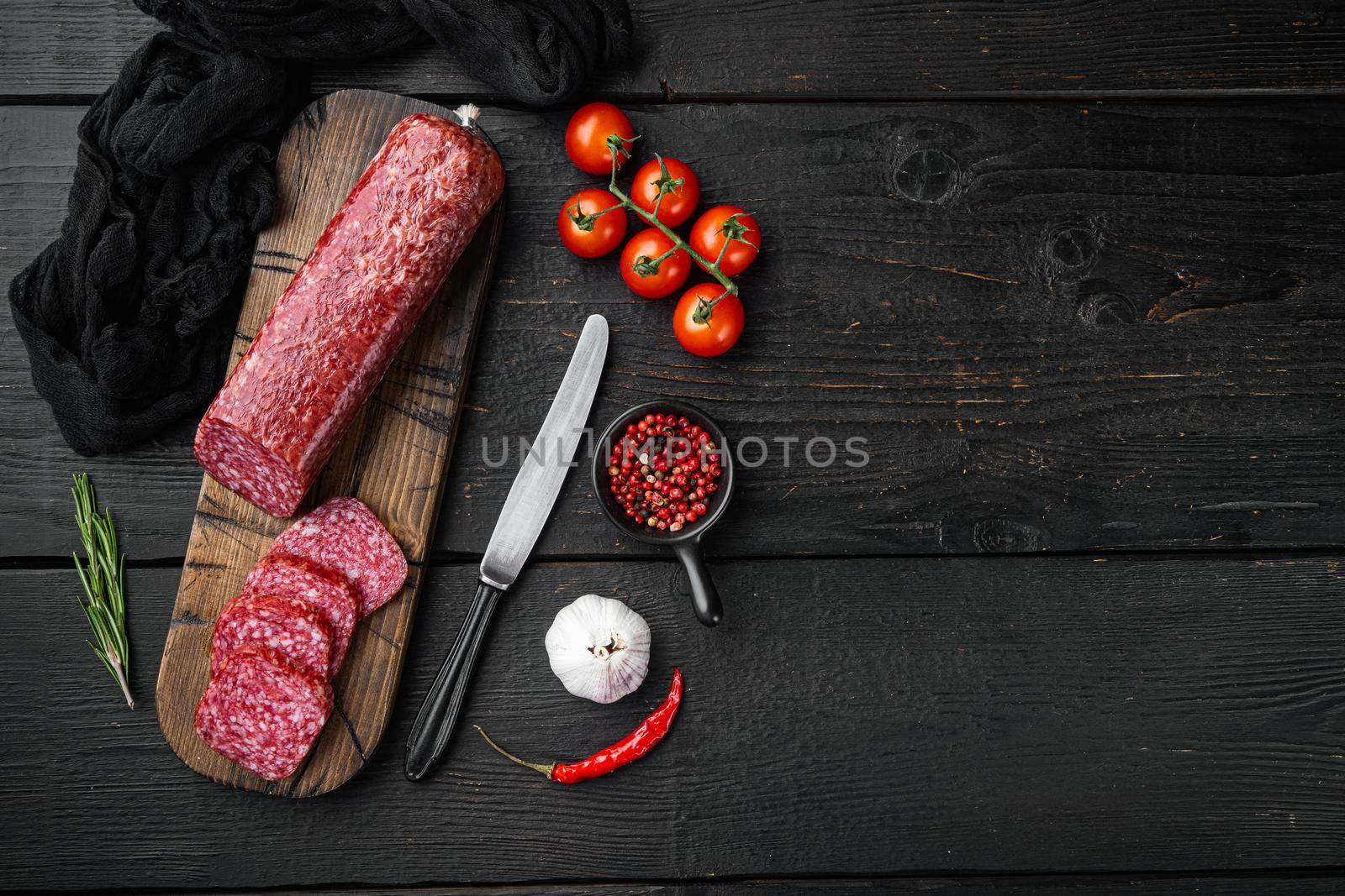 Dry salami sausage with fresh rosemary and spices set, on black wooden table background, top view flat lay, with copy space for text