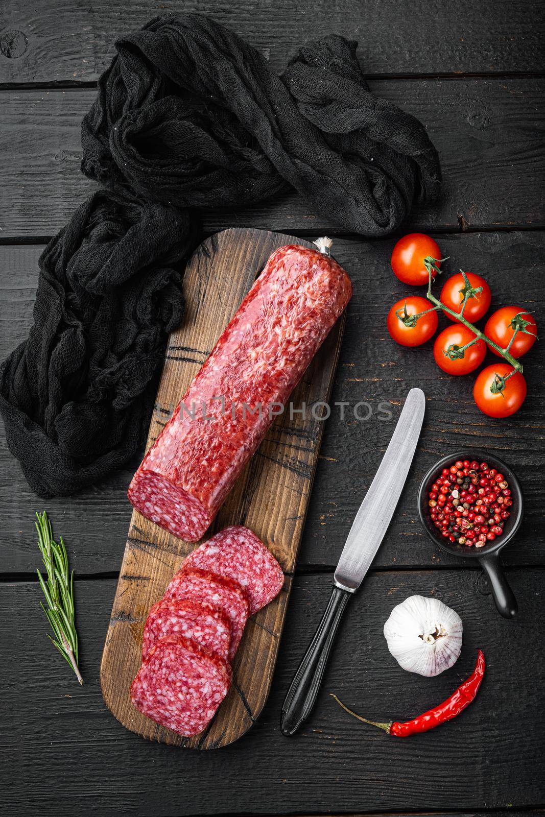 Delicious salami sausage with spices and rosemary set, on black wooden table background, top view flat lay