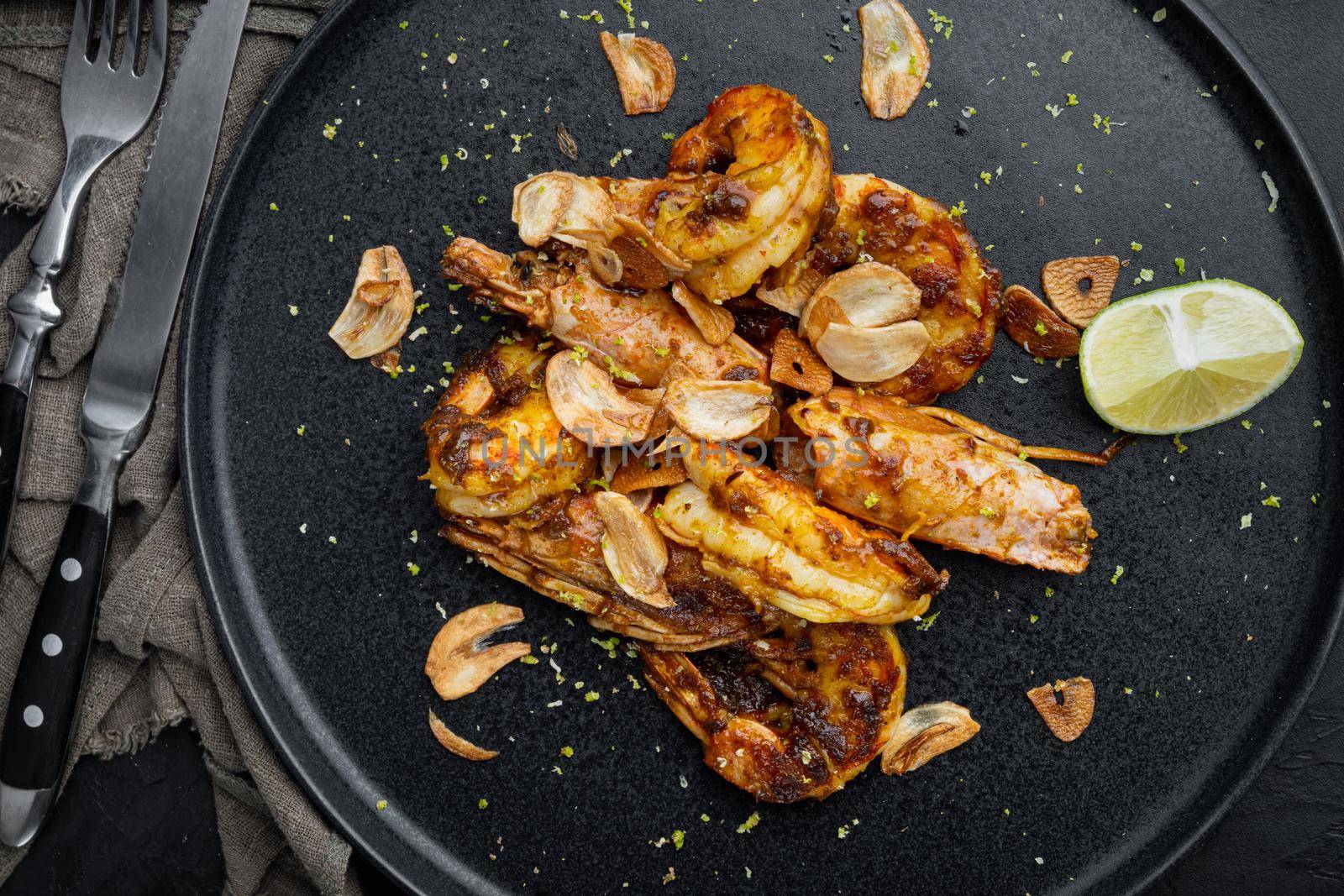 Delicious roasted shrimps with garlic, curry and mango sauce set, on plate, on black background, top view flat lay