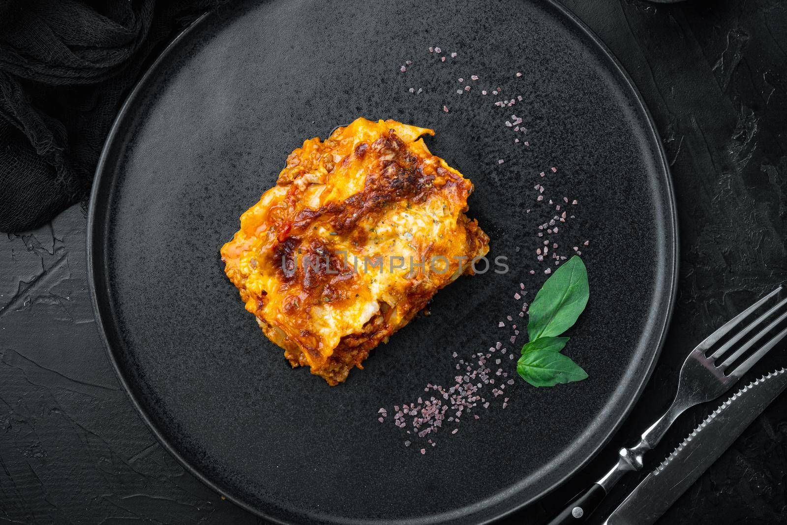Italian Lasagne with tomato bolognese sauce and mince beef meat set, on plate, on black stone background, top view, flat lay