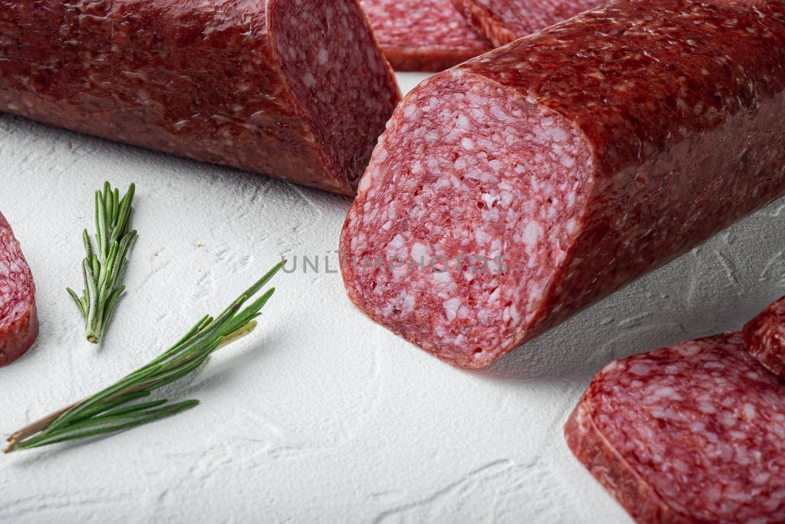 Delicious salami sausage with spices and rosemary set, on white stone table background, with copy space for text