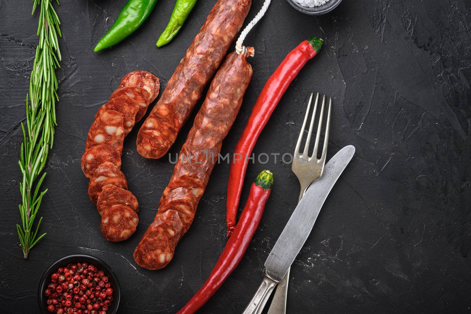 Spanish chorizo sausage slices with herbs and spices on balck background, top view with copy space.