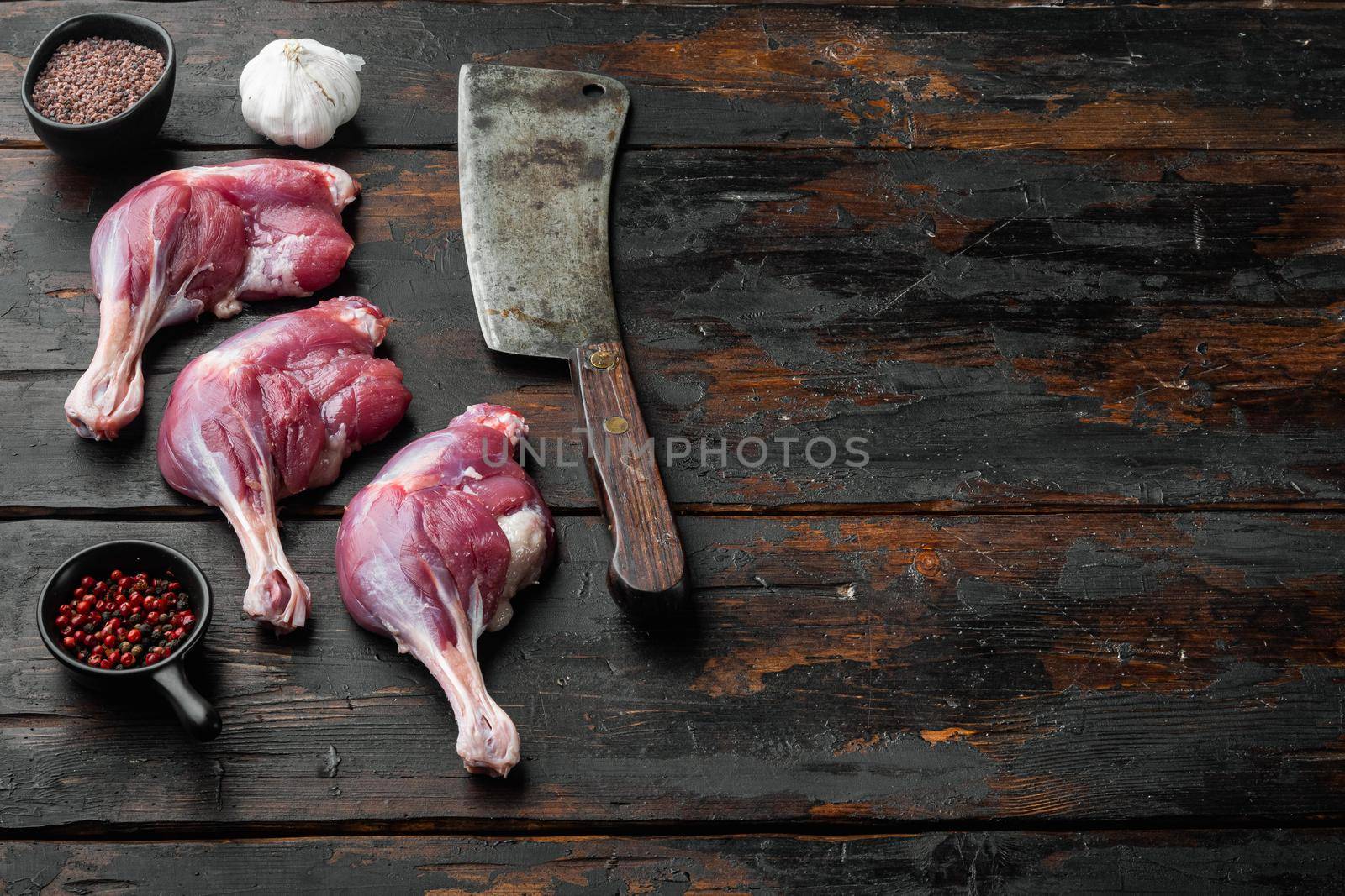 Fresh duck leg meat thighs set with old butcher cleaver knife, on old dark wooden table background, with copyspace and space for text