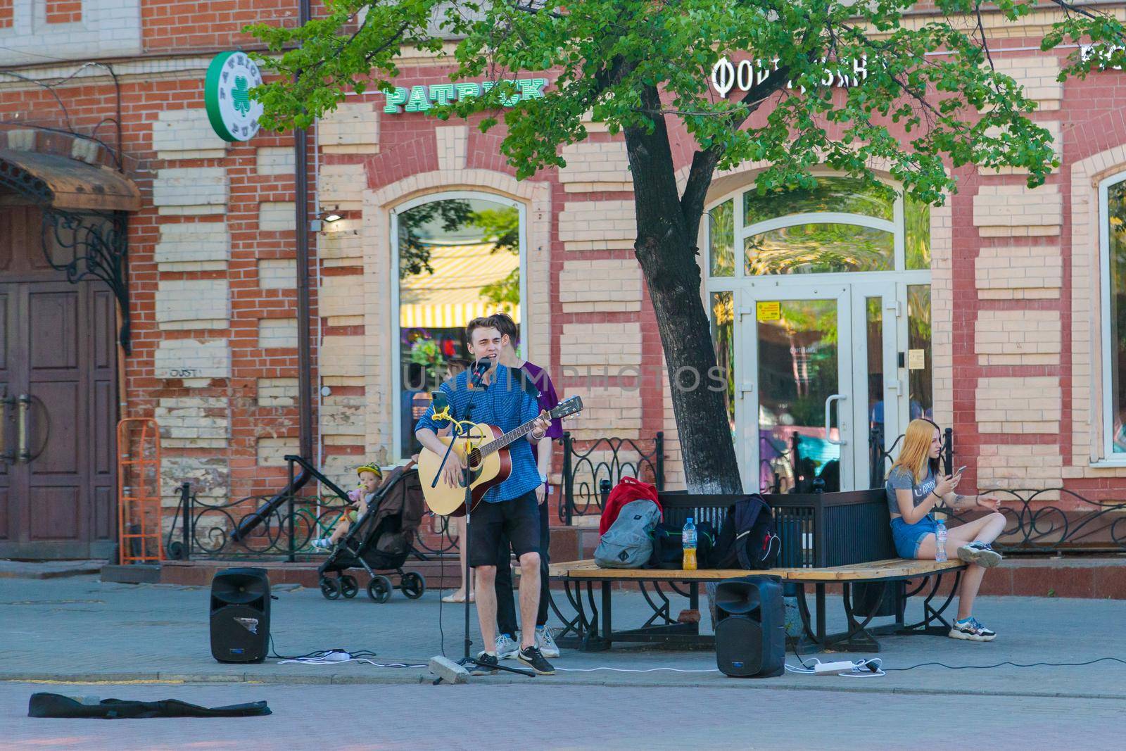 A young guy stands with a guitar on a central street, plays and sings by Yurich32