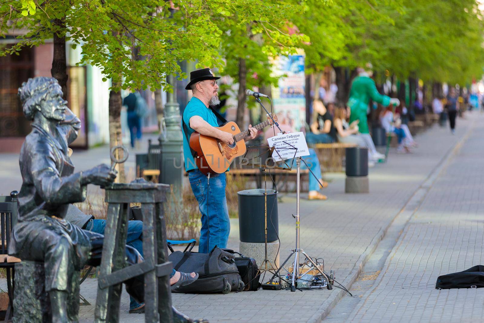 An adult gray-haired man plays guitar and sings on a city street. Street musician. Chelyabinsk, Russia, May 17, 2021