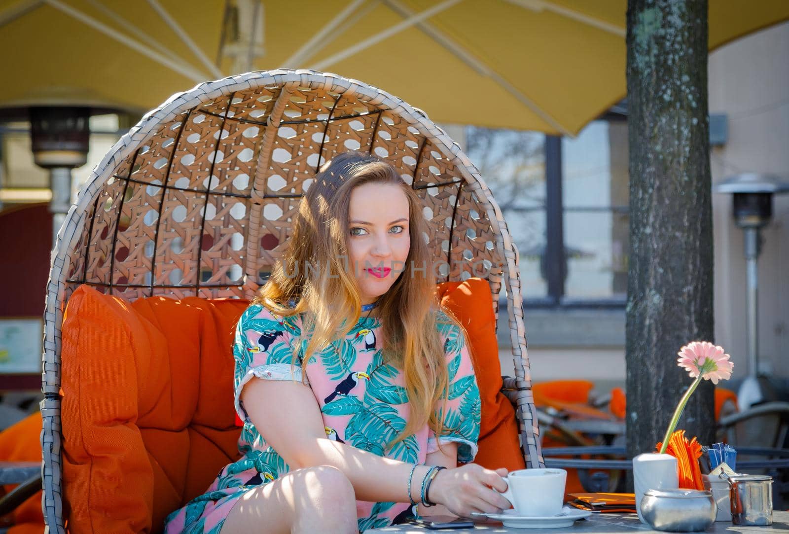 A young girl sits at a table on the terrace with a cup of coffee. Summer, travel