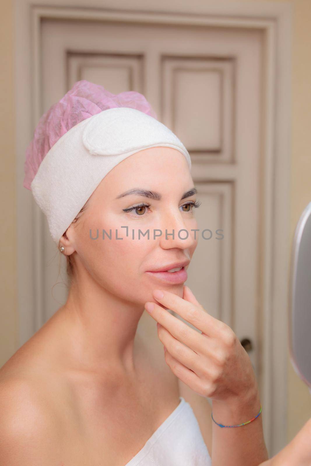 A young girl looks at her face in the mirror after a massage. Happy smile.
