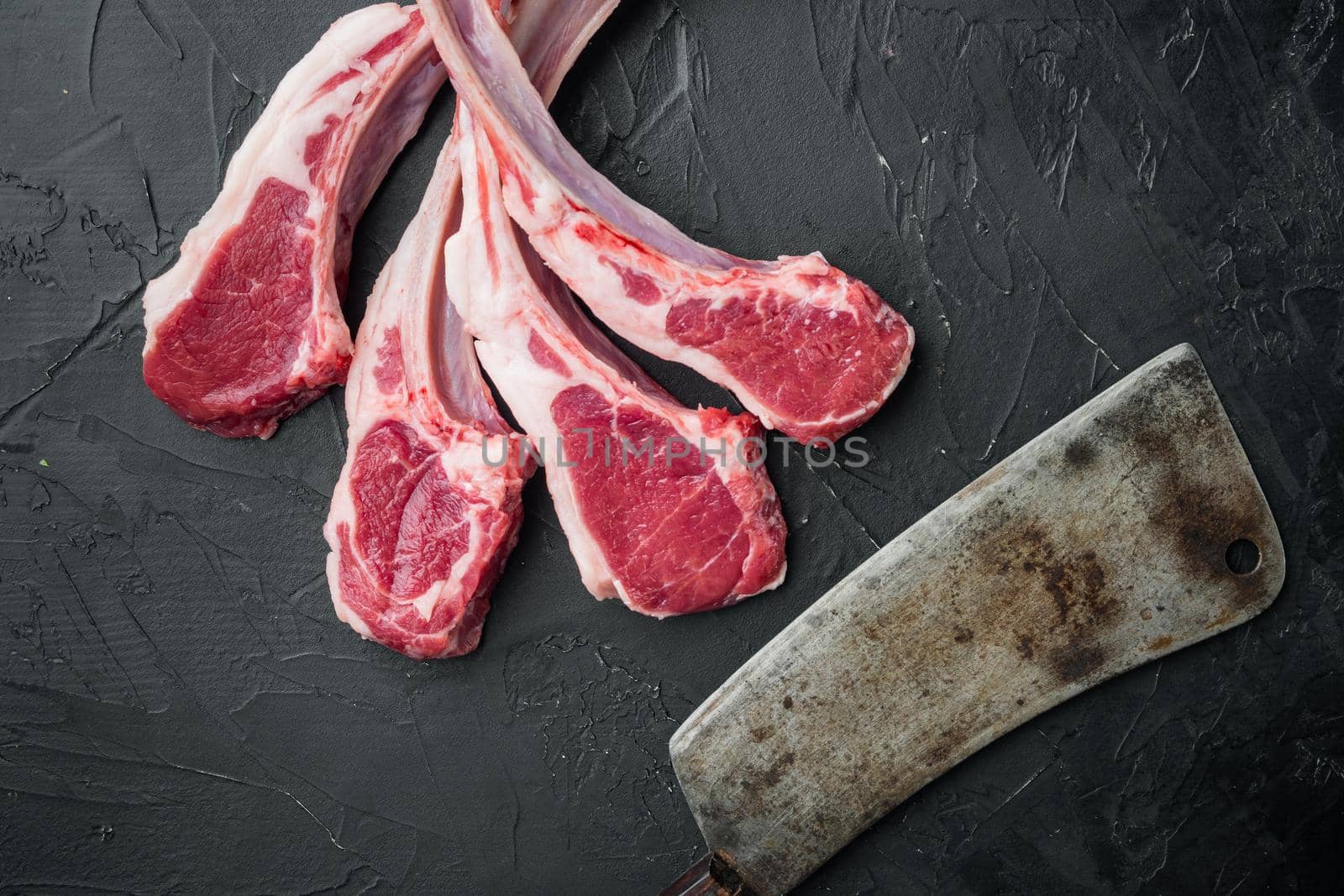 Fresh chopped calf Racks of lamb ready for cooking set, and old butcher cleaver knife, on black stone background, top view flat lay , with copyspace and space for text