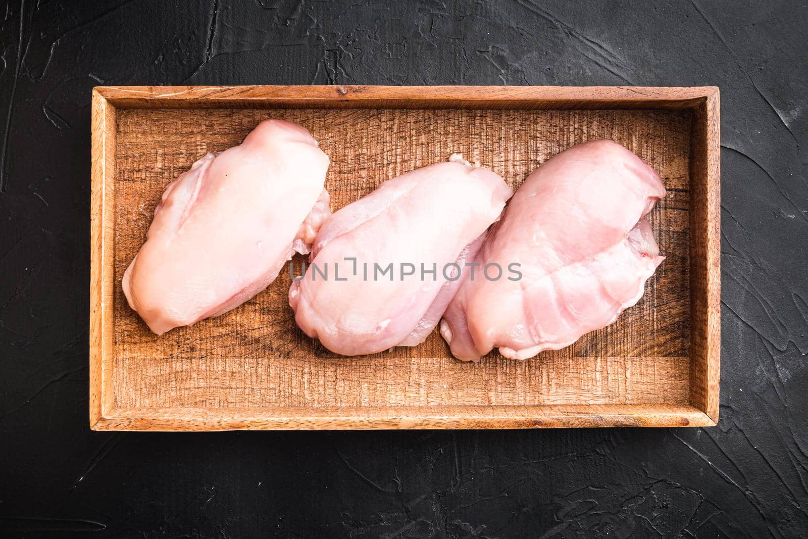 Fresh chicken meat set, in wooden box, on black stone background, top view flat lay